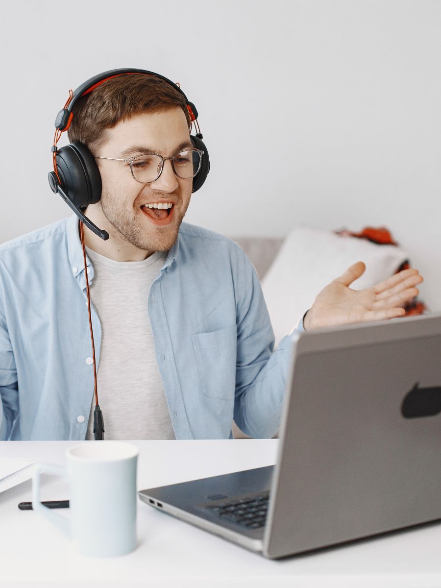 Person mit Headset sitzt vor einem Laptop und gestikuliert während eines Online-Gesprächs.