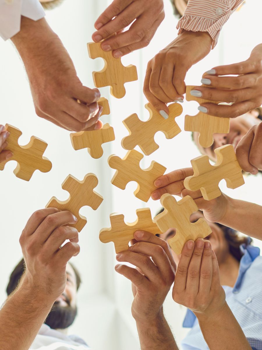 Mehrere Hände halten große hölzerne Puzzleteile in die Mitte.